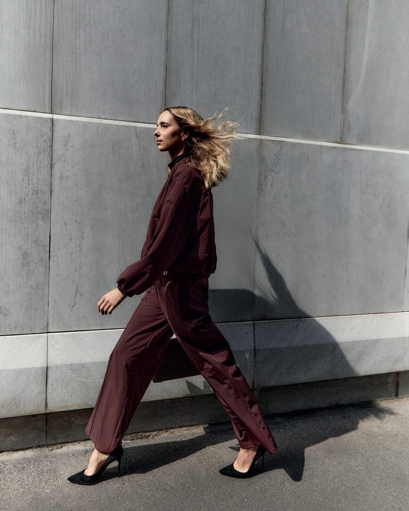 Modella in completo bordeaux cammina lungo un muro grigio, lookbook Ciaogym FW27