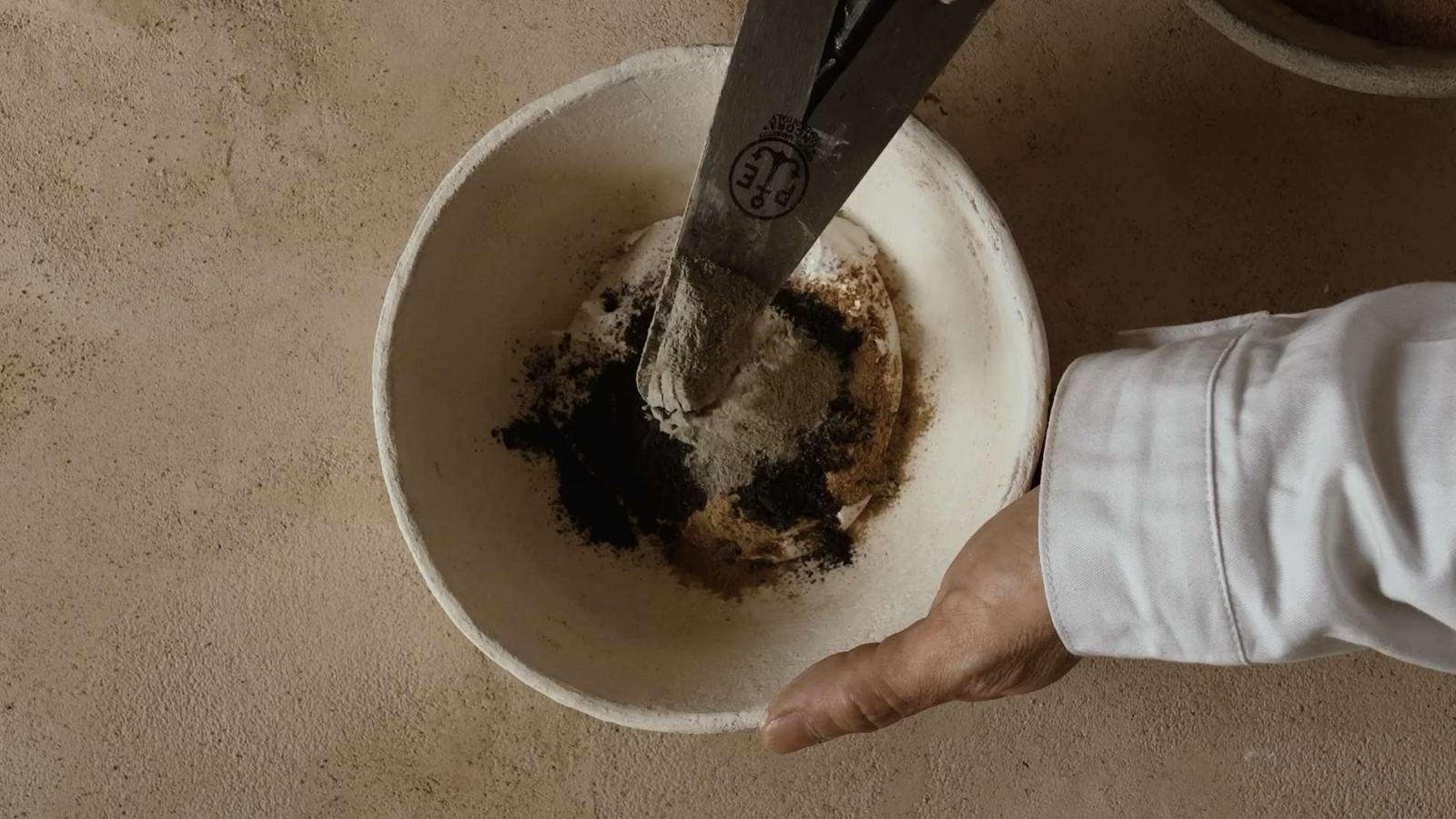 Mani di artigiano che miscelano l'impasto romano per Giorgetti