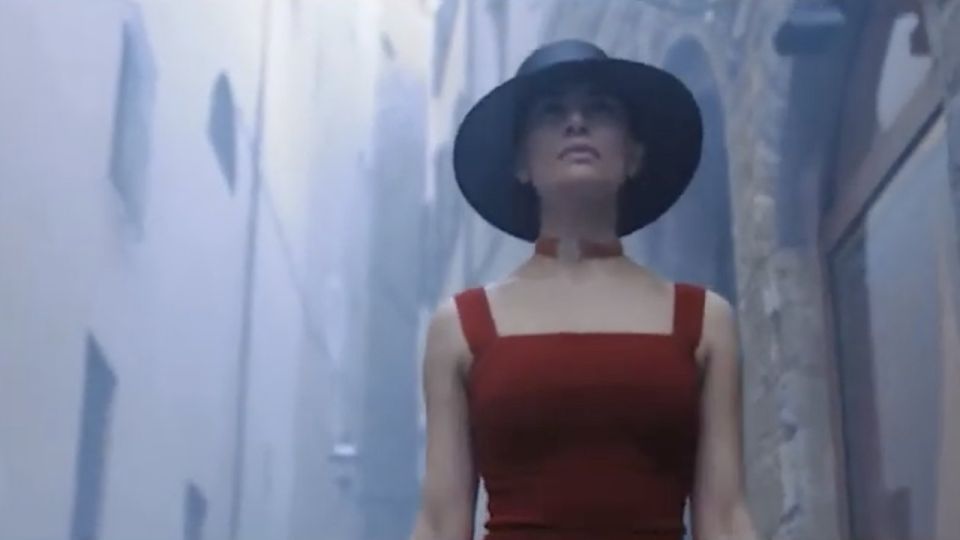 Donna in abito rosso e cappello nero in un vicolo, dal fashion movie Cinque per Cuoio di Toscana